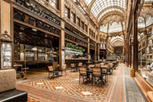The historic glass-domed passage of Párisi Udvar Hotel Budapest, showcasing intricate Moorish-Gothic architecture, mosaic floors, and the elegant Párisi Passage Café.