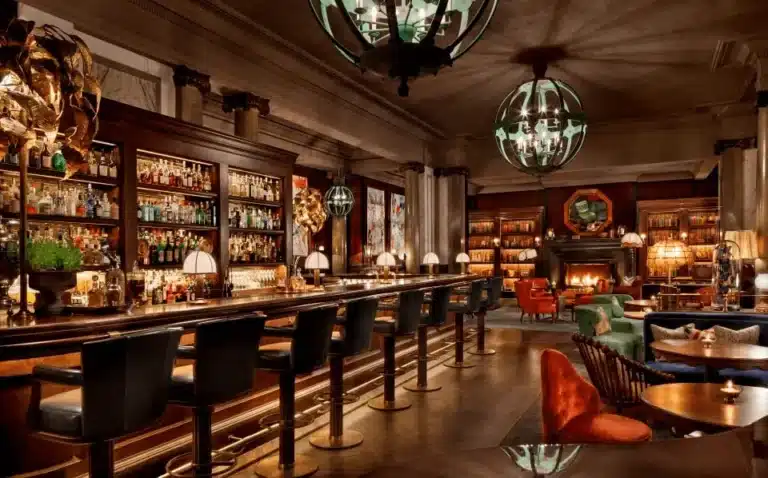 The award-winning Scarfes Bar at Rosewood London, a sophisticated club-style library bar featuring mahogany shelving, a roaring fireplace, and original satirical illustrations by legendary British artist Gerald Scarfe.