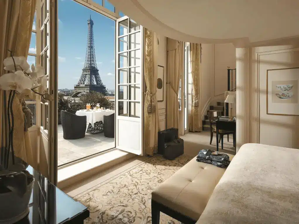 A view from a luxury guest suite at Shangri-La Paris, featuring an open balcony with a breakfast table and a direct, framed view of the Eiffel Tower, housed in the former 19th-century palace of Prince Roland Bonaparte.