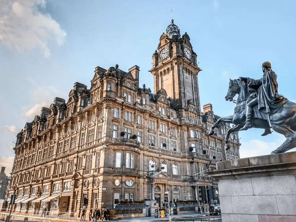 The grand Victorian sandstone facade of The Balmoral Hotel in Edinburgh, featuring its iconic 190-foot clock tower and ornate Scots Baronial architecture, situated at the prominent corner of Princes Street and North Bridge.
