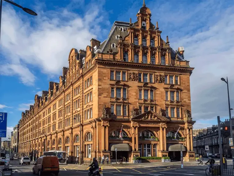 The grand Renaissance Revival-style red sandstone facade of The Caledonian Edinburgh, built in 1903 as a premier railway hotel, featuring three magnificent entrance arches that originally provided street-level access to the Princes Street Station platforms.