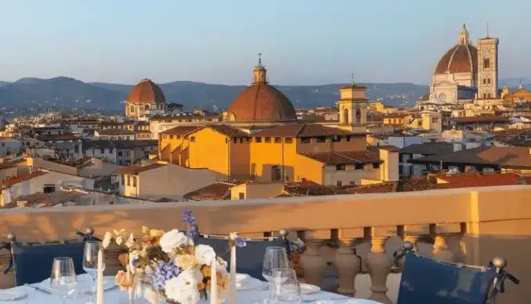 A view from the rooftop of The Excelsior Hotel Florence, a 19th-century landmark in Piazza Ognissanti, showing a dining terrace overlooking the Renaissance skyline, including the iconic red-tiled Duomo and Giotto's Bell Tower.