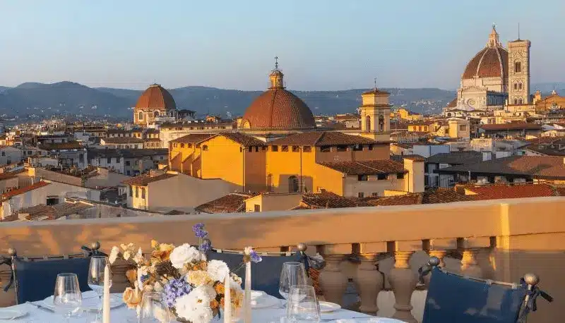 A view from the rooftop of The Excelsior Hotel Florence, a 19th-century landmark in Piazza Ognissanti, showing a dining terrace overlooking the Renaissance skyline, including the iconic red-tiled Duomo and Giotto's Bell Tower.