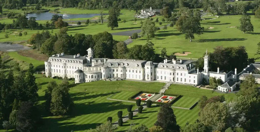An aerial view of The K Club in Kildare, showing the 19th-century French-style Straffan House with its symmetrical stone pavilions and mansard roofs, surrounded by manicured lawns, formal gardens, and championship golf courses designed by Arnold Palmer.