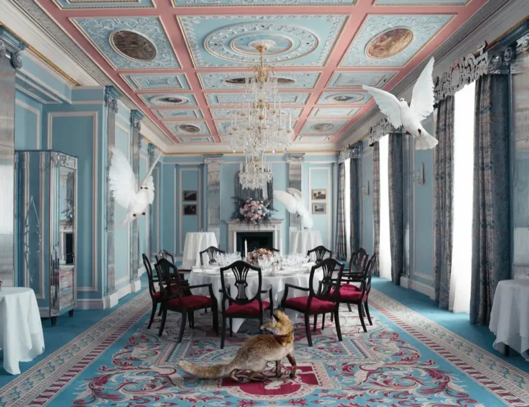 An opulent Regency-style dining room at The Lanesborough London featuring a pastel blue and pink coffered ceiling with gold-leaf detailing, a grand crystal chandelier, and walls adorned with 18th-century artwork.