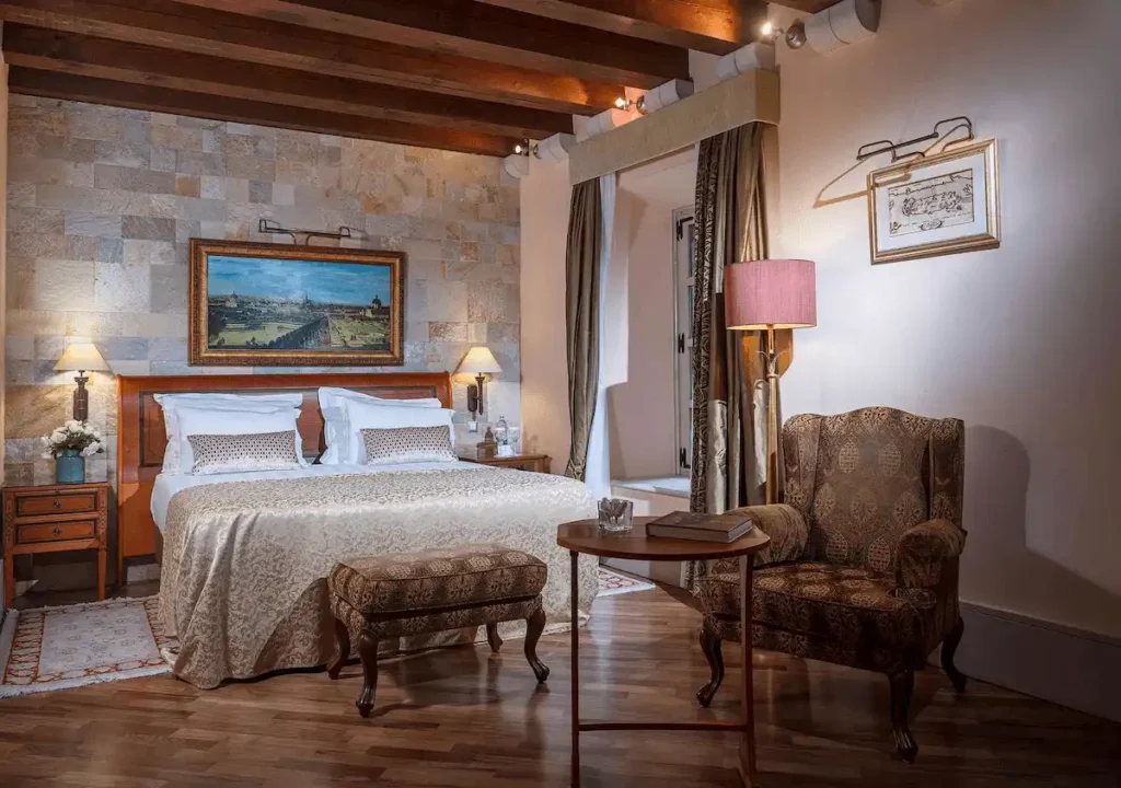 A luxury guest room at The Pucic Palace featuring authentic 18th-century stone walls, original dark wood ceiling beams, and classical aristrocratic furnishings in Dubrovnik's Old Town.