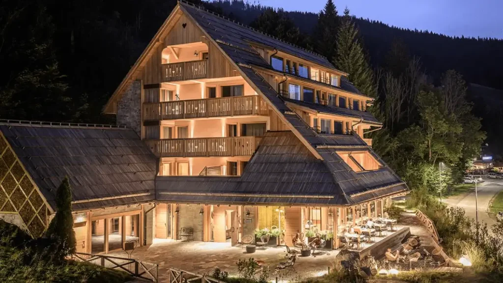 The illuminated timber facade of Vila Planinka at twilight, a 5-star boutique hotel in the Jezersko Alps featuring organic architecture, natural energy points, and a zero-electronics digital detox concept.
